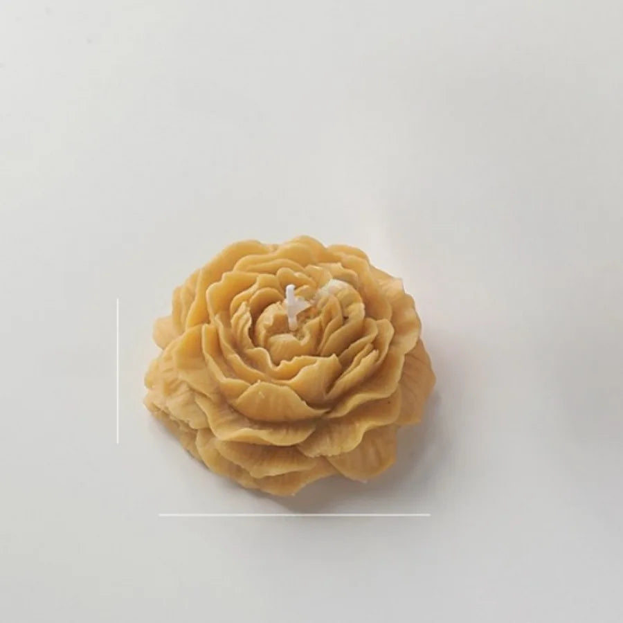 Golden-yellow, rose-shaped candle with intricate, layered petals and a centered wick on a plain white background.