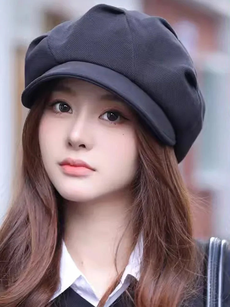 A woman wearing a classic black, structured newsboy beret with a curved peak and textured fabric finish.
