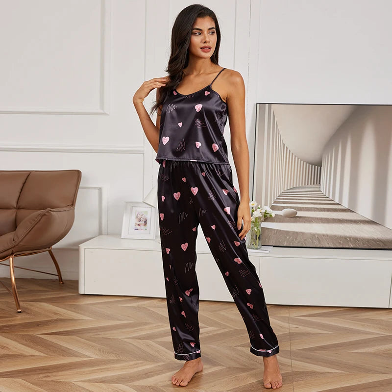 Woman wearing black satin pyjama set with pink heart pattern, featuring a camisole top and matching long trousers.