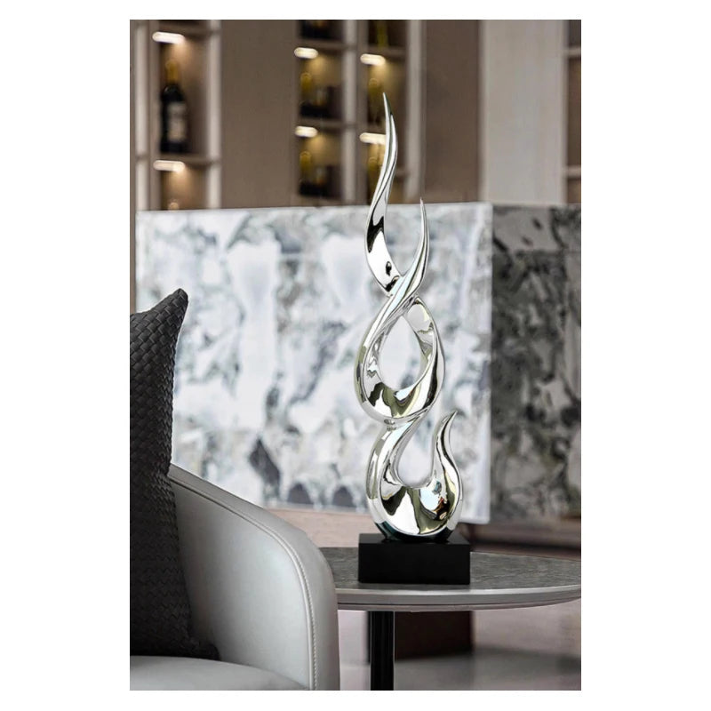 A modern, silver-coloured abstract resin sculpture with a flame-like design on a sleek black square base.