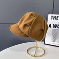Tan retro newsboy beret in a textured fabric, displayed on a gold stand.