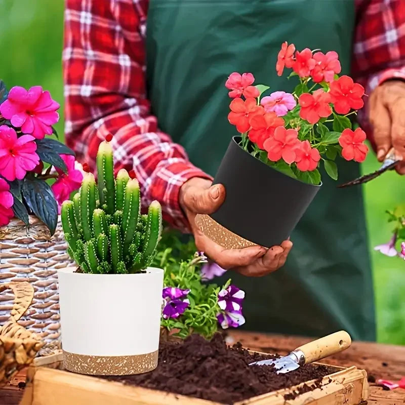 A gardener holding a black planter with red flowers, next to a white planter with a cactus. Both pots have cork bases.