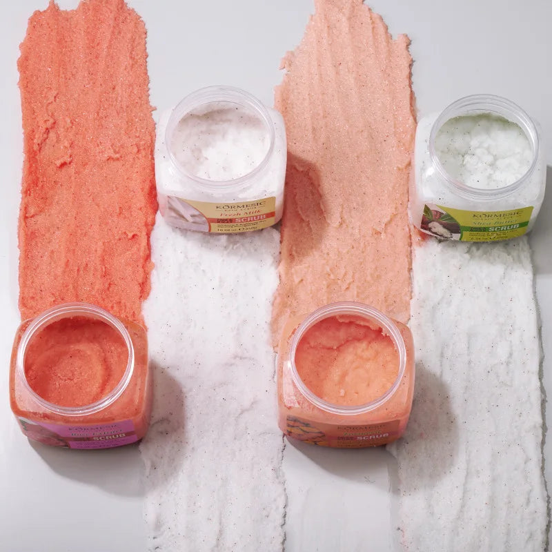 Four open tubs of exfoliating body scrub with colourful paste swatches in pink, peach, and white textures.