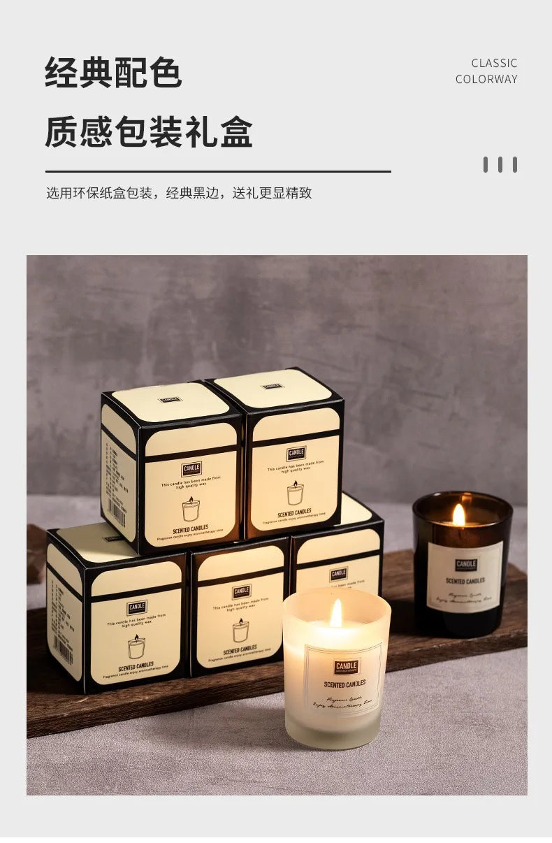 Cream and black scented candle gift boxes with two lit candles in frosted and amber glass jars on a wooden tray.