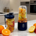 Portable personal blender with a navy base, copper trim, and clear blending jar filled with fruit, plus a spare cup.