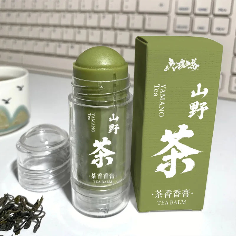 Green tea solid balm stick in a clear twist-up tube, next to its matching green box with white text.