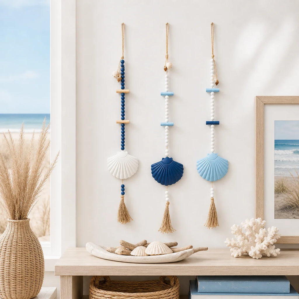 Three boho wall hangings with blue, white, and wood beads, large shell pendants, and jute tassels on a white wall.