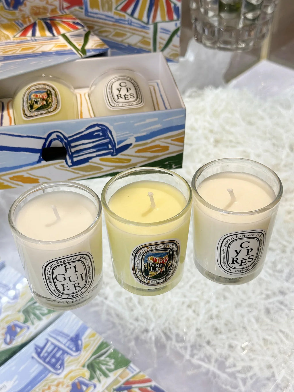 Three mini scented candles in clear glass votives, presented in a decorative box with beach-themed artwork.