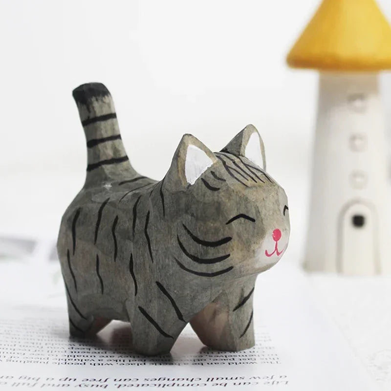 Small, hand-carved grey tabby cat figurine with a smiling face and upright tail, standing on a book.
