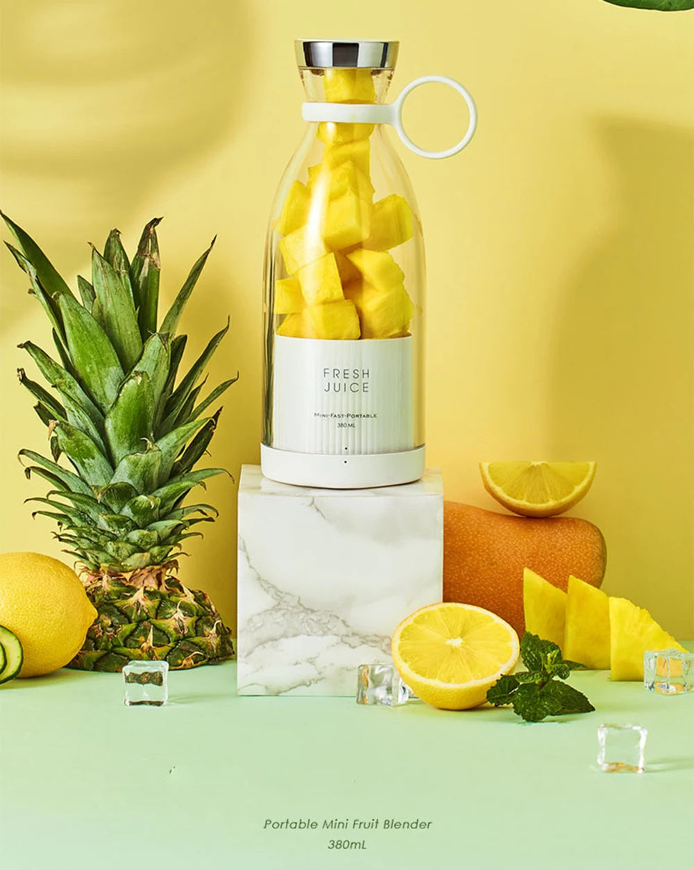 White portable mini blender filled with pineapple chunks, displayed on a marble stand with fresh fruit and ice cubes.