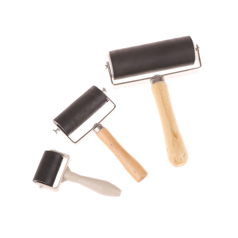 Set of three black rubber craft brayer rollers with wooden and light grey handles, isolated on a white background.