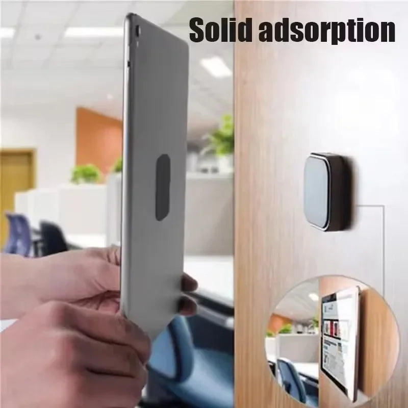 A small, square, grey magnetic wall mount holding a silver tablet vertically against a wooden surface.