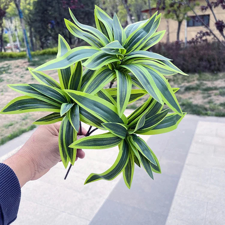 A hand holds a bunch of artificial, spiky lily-like plants with vibrant green and lime striped leaves outdoors.