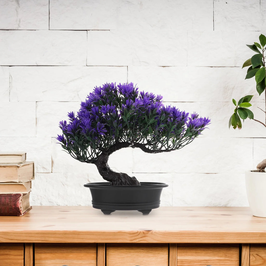 Artificial purple bonsai tree in a black oval pot on a wooden table, with white brick wall background.