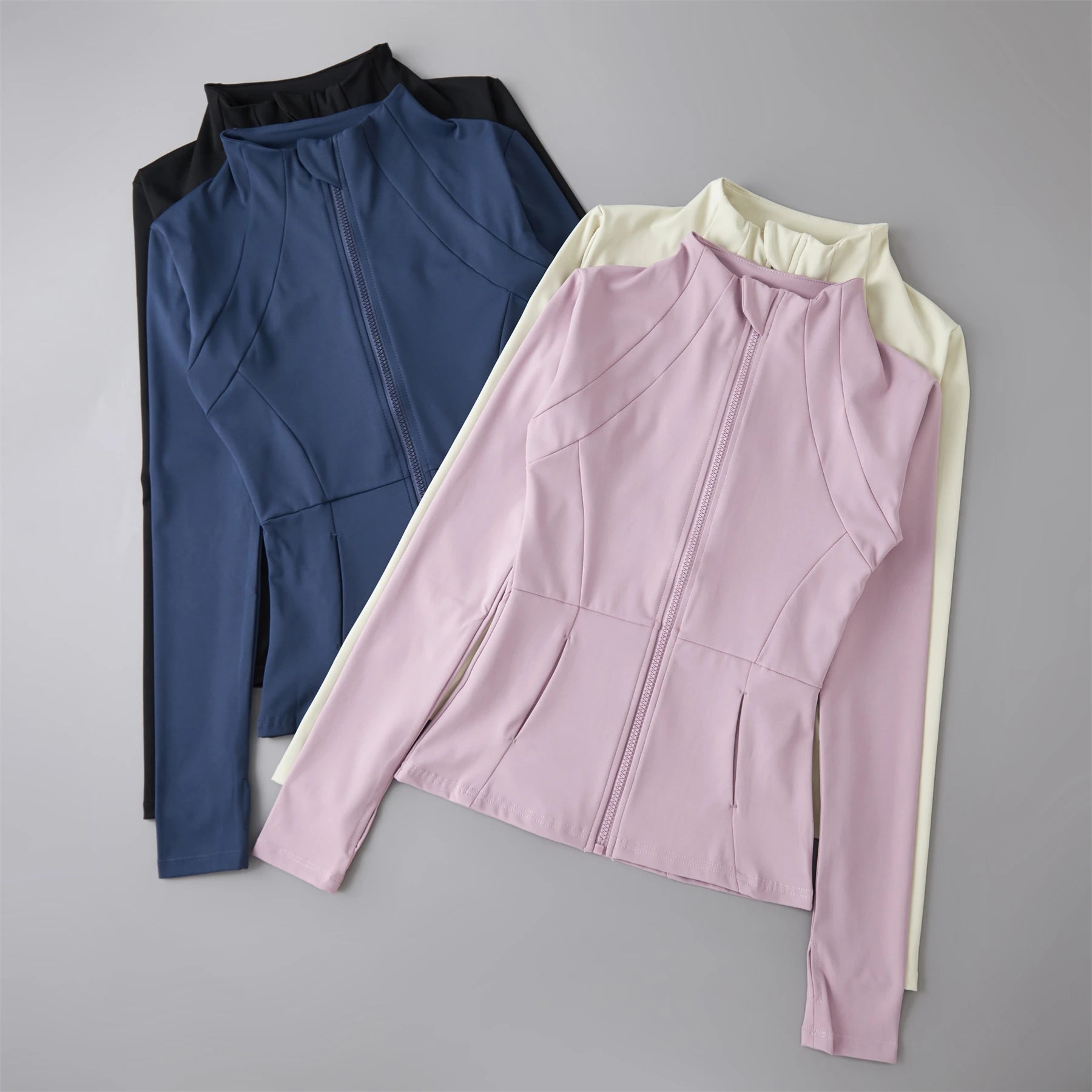 Four zip-up athletic jackets with high collars in black, blue, pink, and cream, featuring seam detailing and long sleeves.