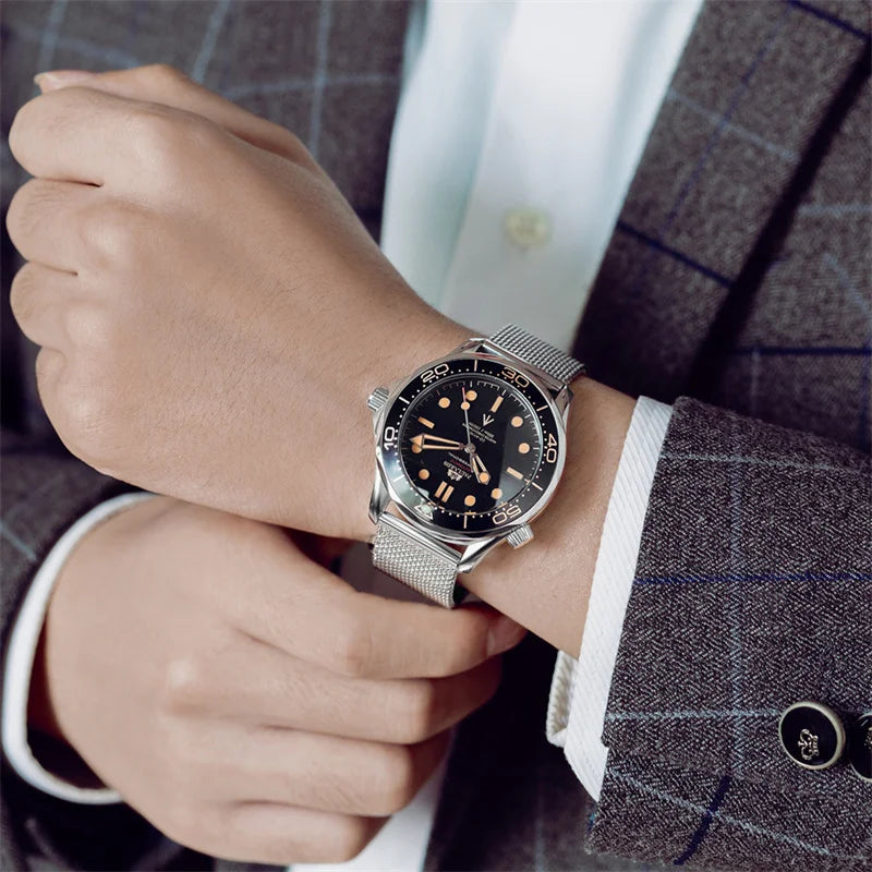 A classic men's automatic watch with a black dial, gold markers, and a silver stainless steel mesh strap on a wrist.