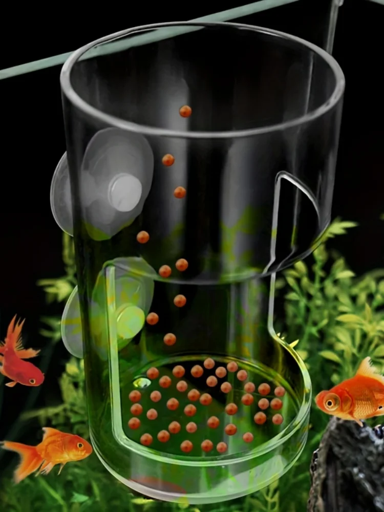 Clear acrylic fish feeder with suction cups, mounted in an aquarium with orange goldfish pellets falling inside.