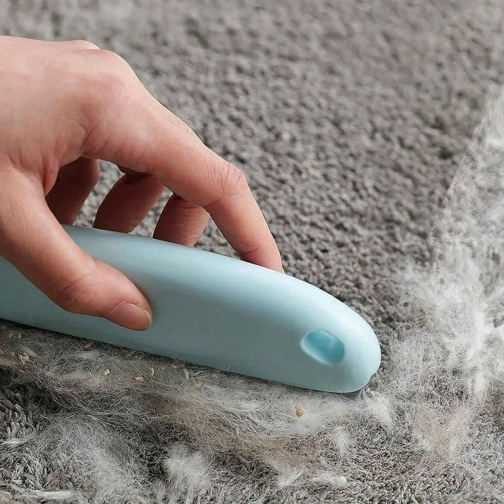 A hand uses a pale blue portable lint remover to clear lint and pet hair from a grey carpet.