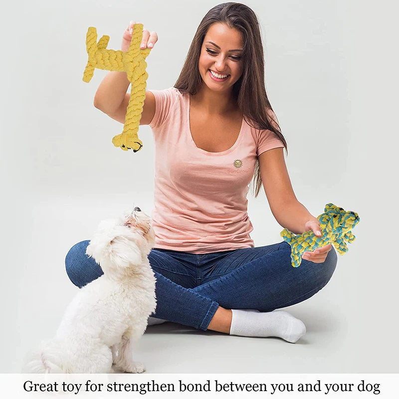 A smiling woman playing with her white dog using two colourful, braided rope animal-shaped dog chew toys.