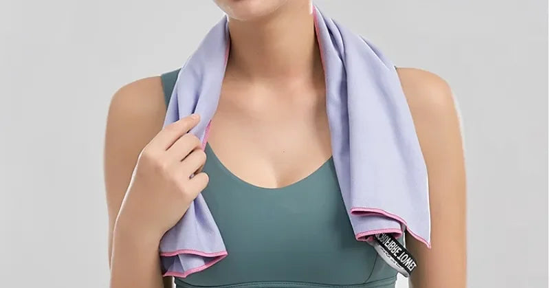 A person wearing a lilac sports towel with contrast pink edging draped around their neck over a dark green gym top.