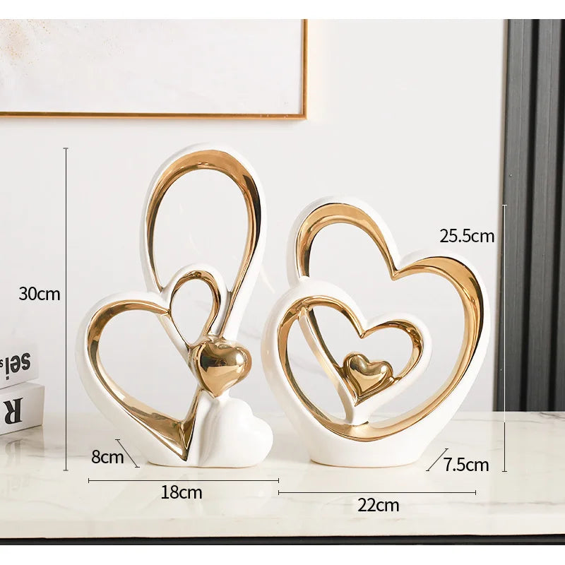 Two modern white and gold ceramic heart sculptures with dimensions displayed on a marble surface.