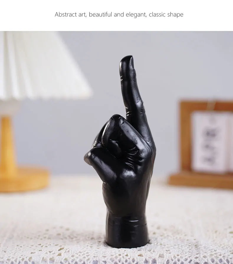 Elegant black matte hand sculpture with index finger pointing upwards, standing on a textured surface.