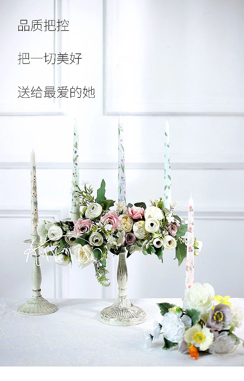 Vintage-style distressed white candlesticks decorated with artificial pink and white roses and floral-patterned candles.