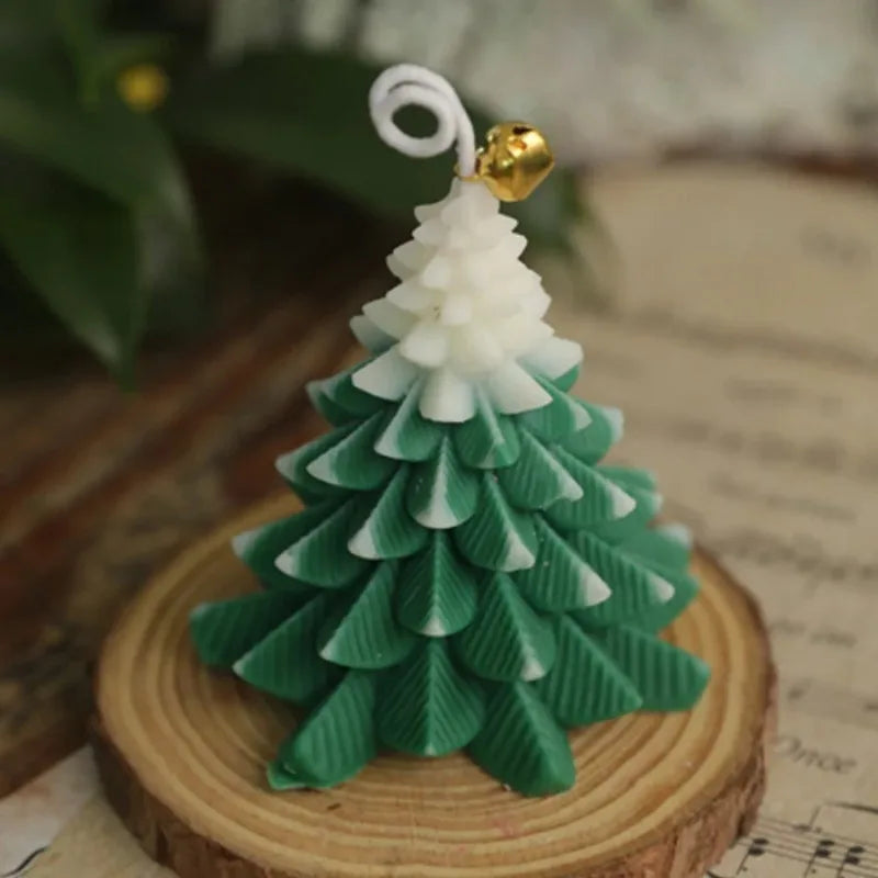 Green and white Christmas tree-shaped candle on a wood slice base, topped with a decorative gold bell.