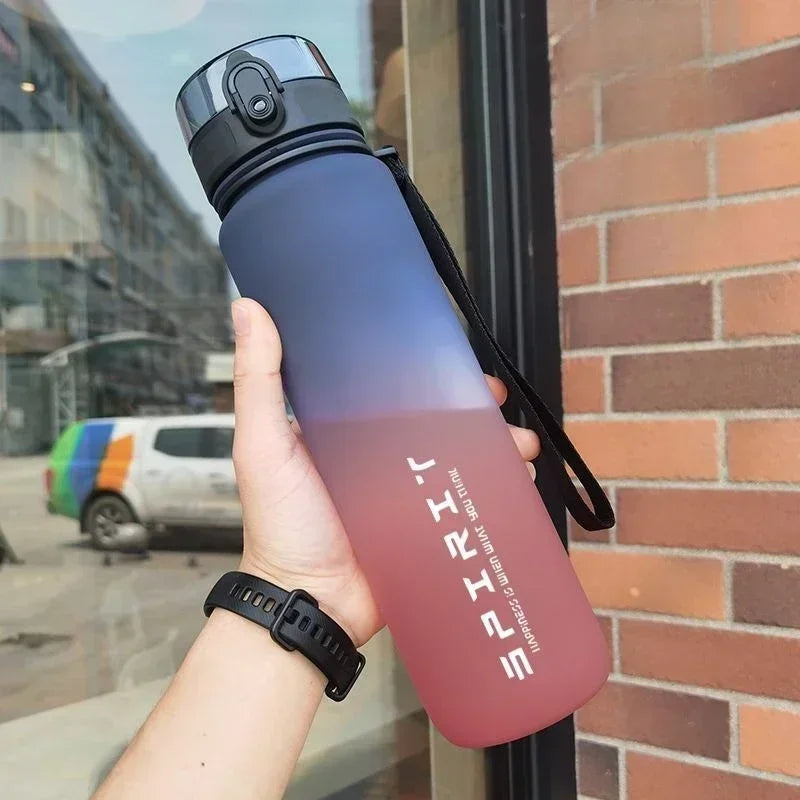A person holding a matte, blue-to-pink gradient sports water bottle with a black lid and carry strap.