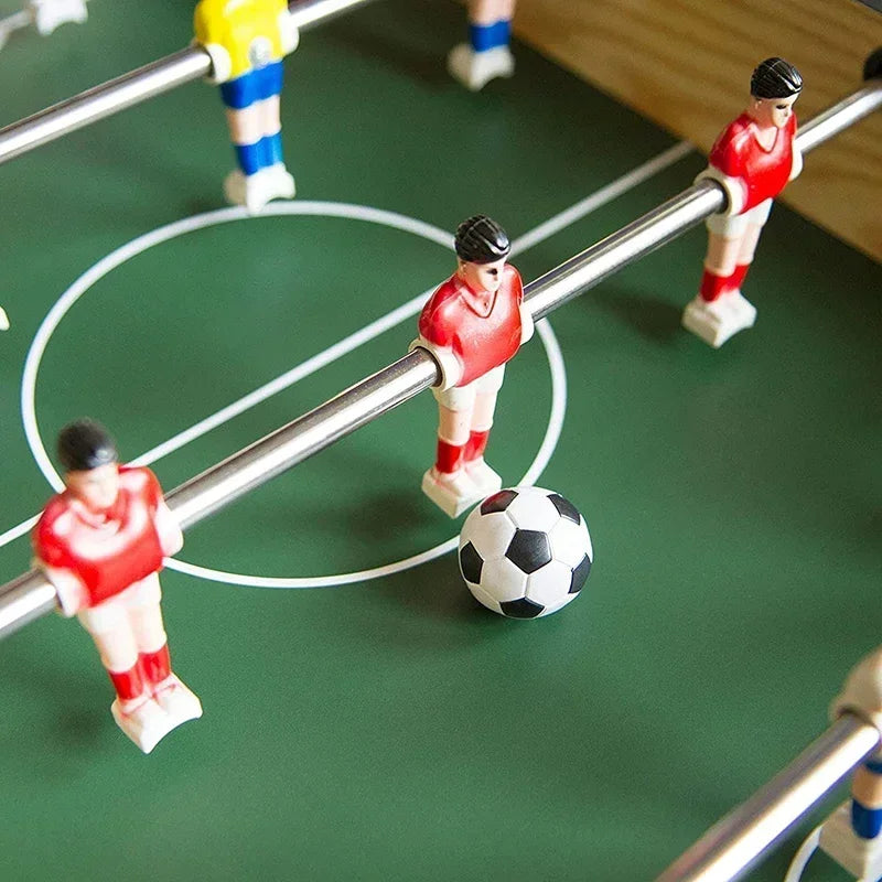 Close-up of a foosball table with green pitch, metal rods, and red and yellow player figurines with a ball.