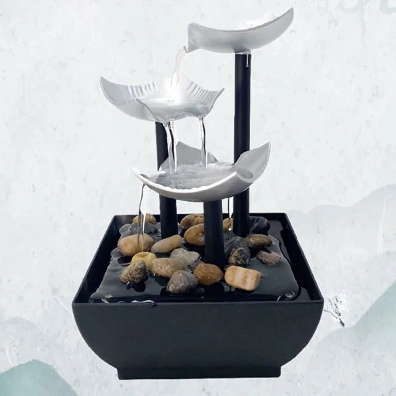 Modern tabletop water fountain with three cascading silver-coloured tiers and a black base filled with decorative stones.
