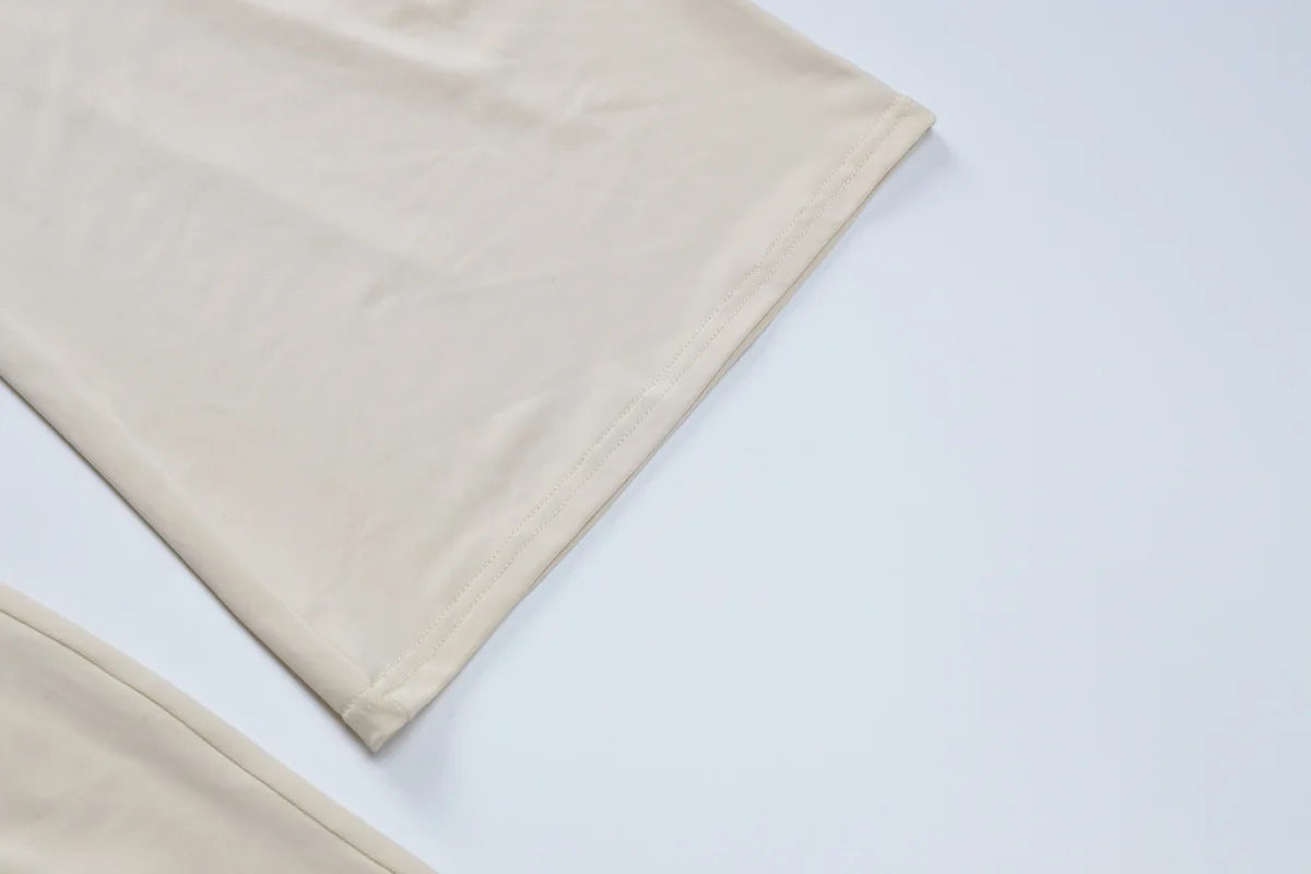 Close-up of a smooth, beige fabric garment with a clean, stitched hem on a plain white background.