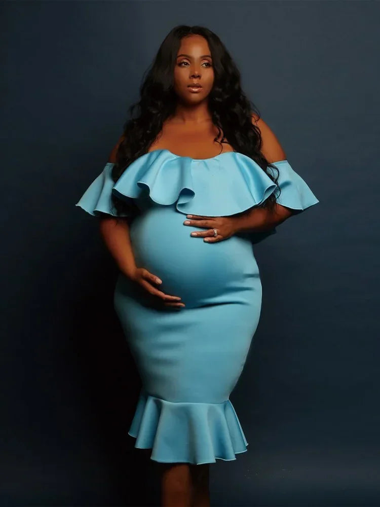 A pregnant woman wearing a light blue, off-the-shoulder maternity dress with ruffle detailing and a mermaid hem.