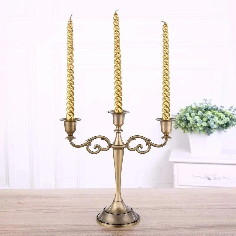 Bronze metal 3-arm candelabra with scroll accents holding three tall, twisted gold taper candles.