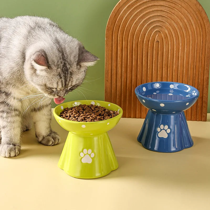 A cat eating from a lime-green, elevated ceramic bowl with white polka dots and a paw print design.