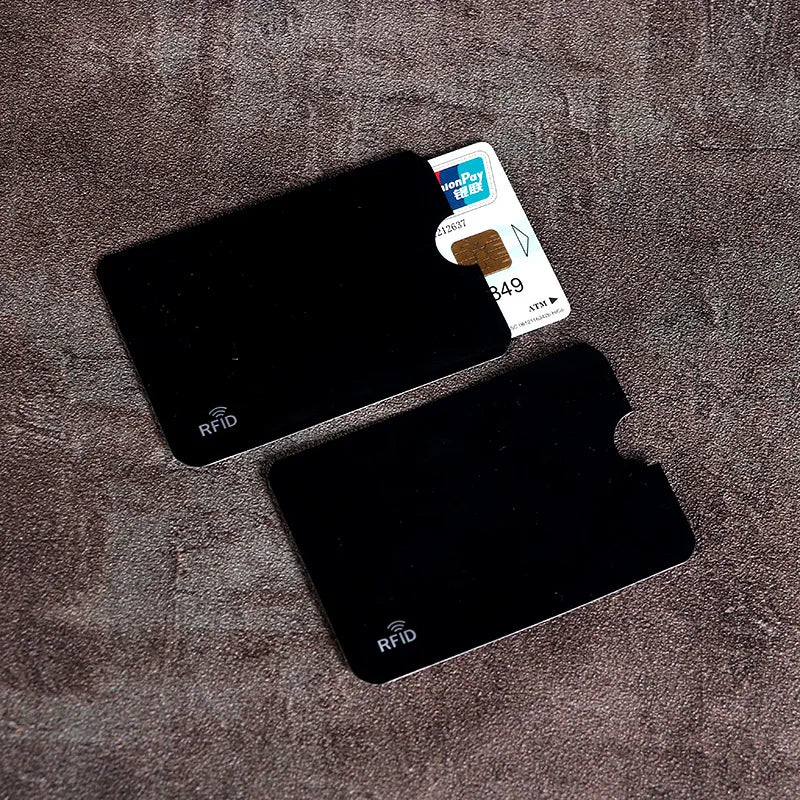 Two black metal RFID-blocking card holders with thumb cutouts, one containing a bank card.