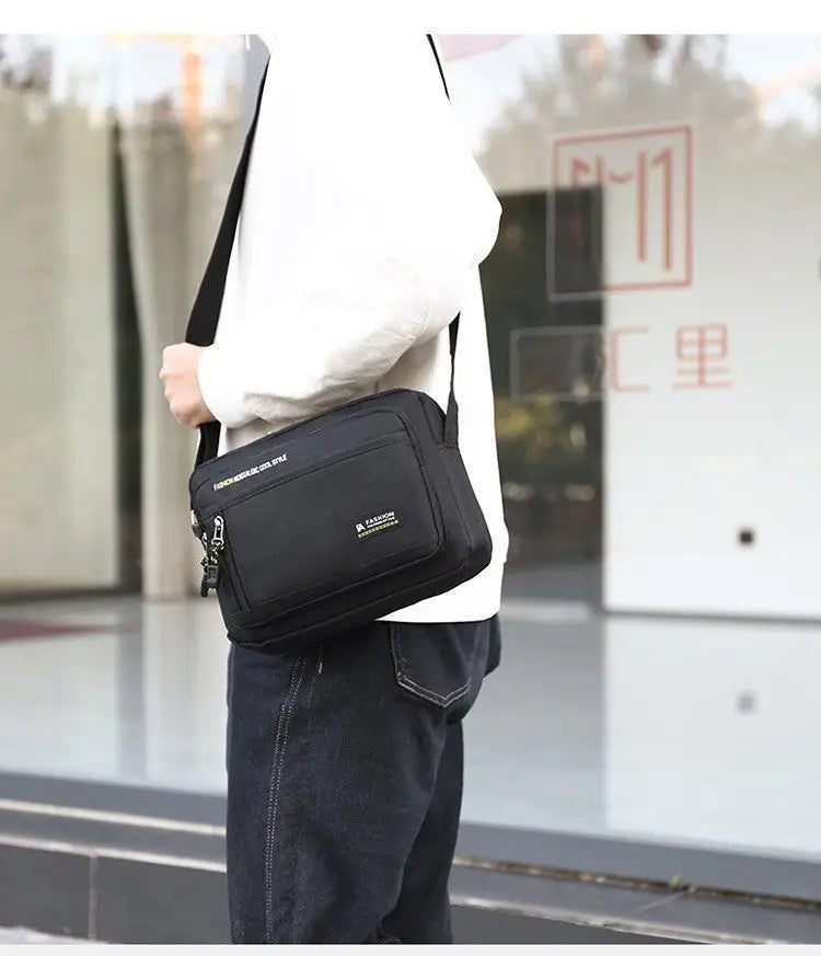 A man wearing a sleek, black rectangular crossbody bag with an adjustable strap, zip pockets, and modern style.