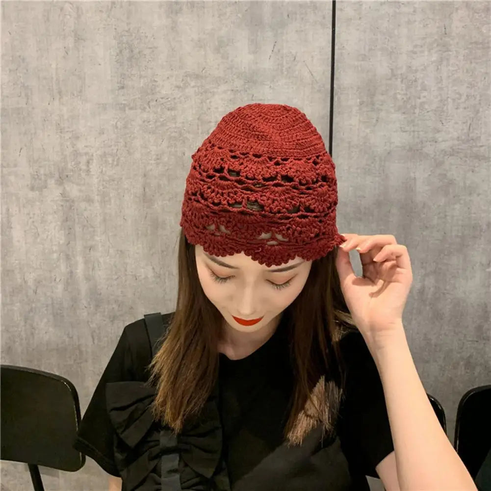 A woman wearing a dark red, hollow-out crochet lace beanie with a decorative scalloped edge.