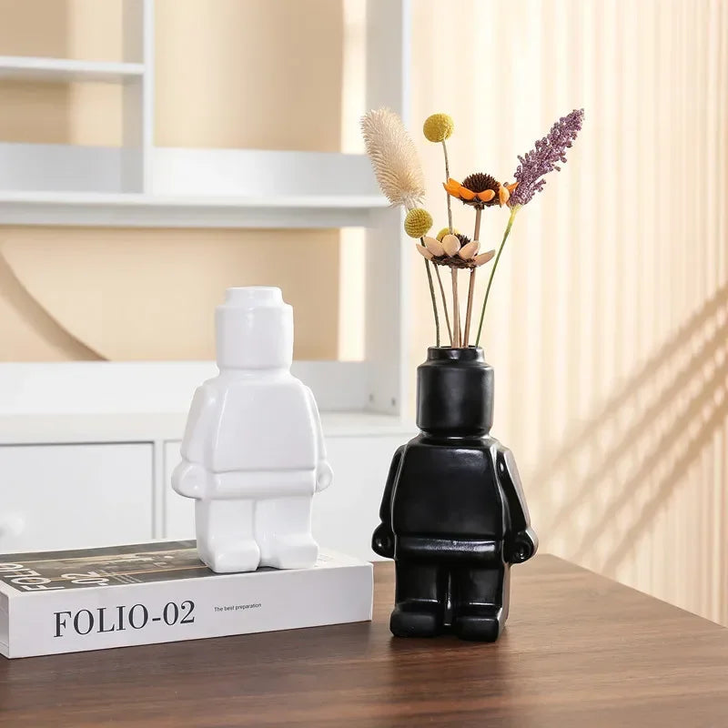 Two modern, minimalist figure-shaped ceramic vases in matte black and white on a wooden table with dried flowers.
