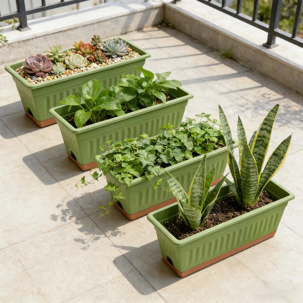 Four green, ribbed rectangle planters with terracotta bases arranged on a tiled balcony, each holding different plants.