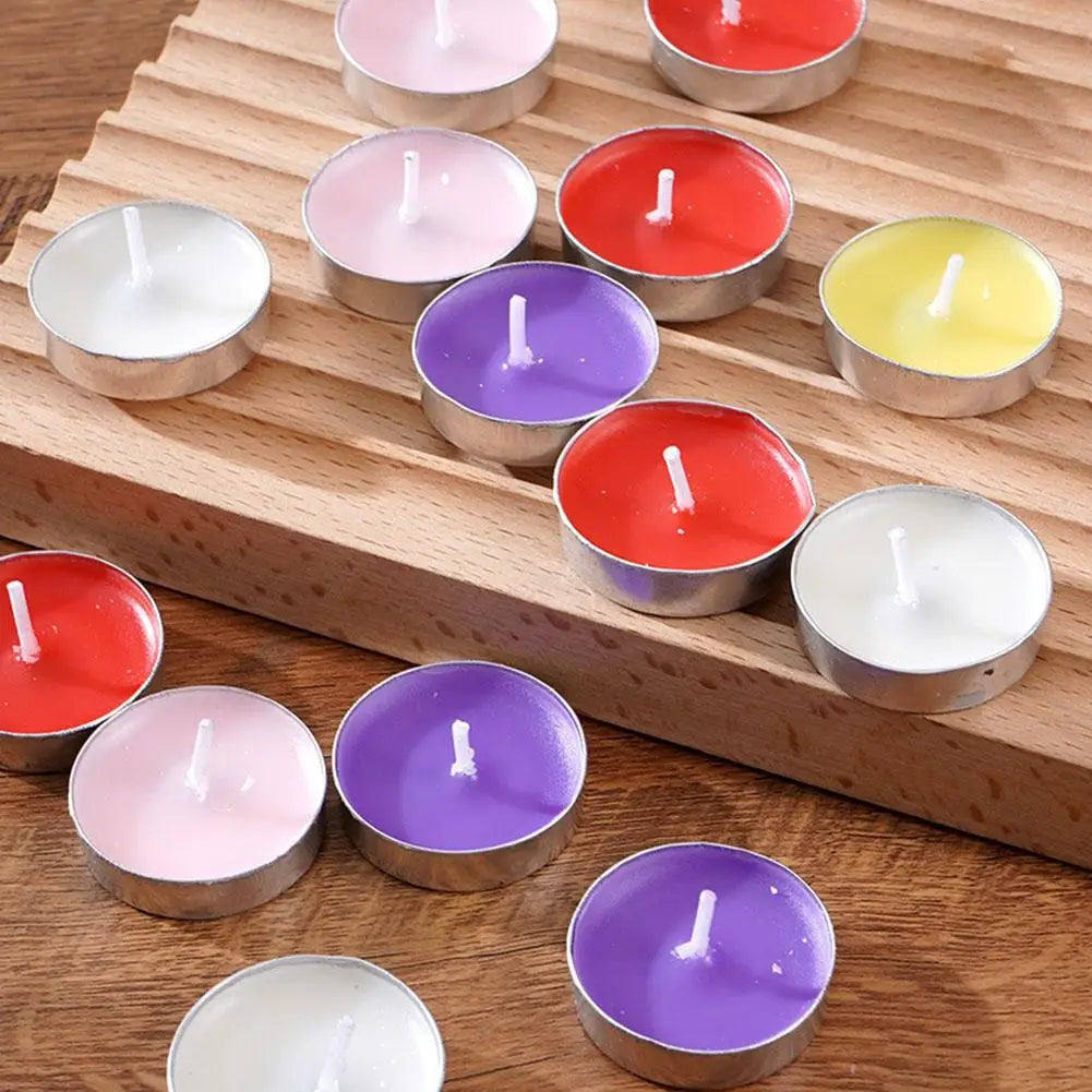 Assorted colourful tealight candles in silver metal cups, arranged on a textured wooden surface.