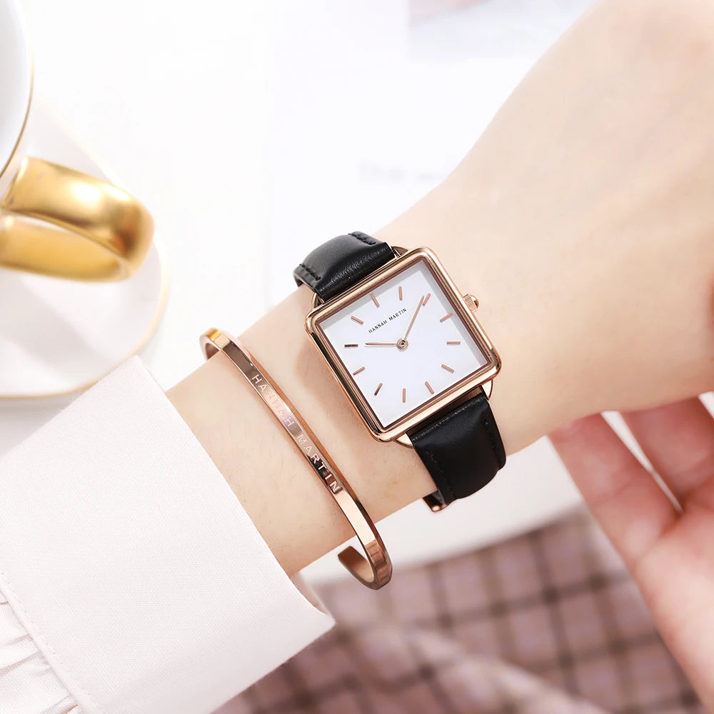 Women's square watch with rose gold case, white dial, and black leather strap, worn with a matching cuff.
