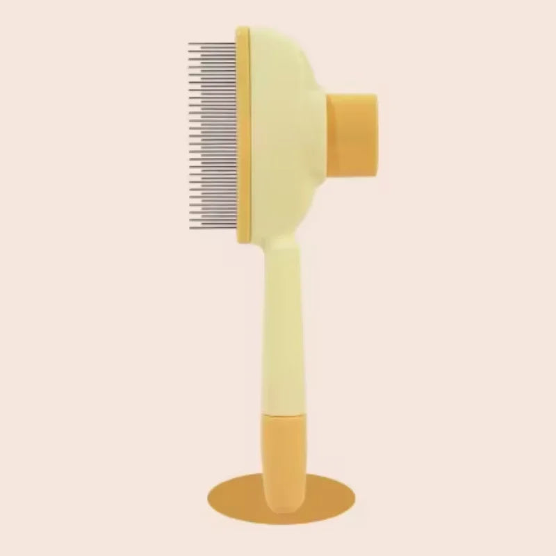 Pale yellow and orange pet grooming brush with fine metal teeth, standing upright on a matching round base.