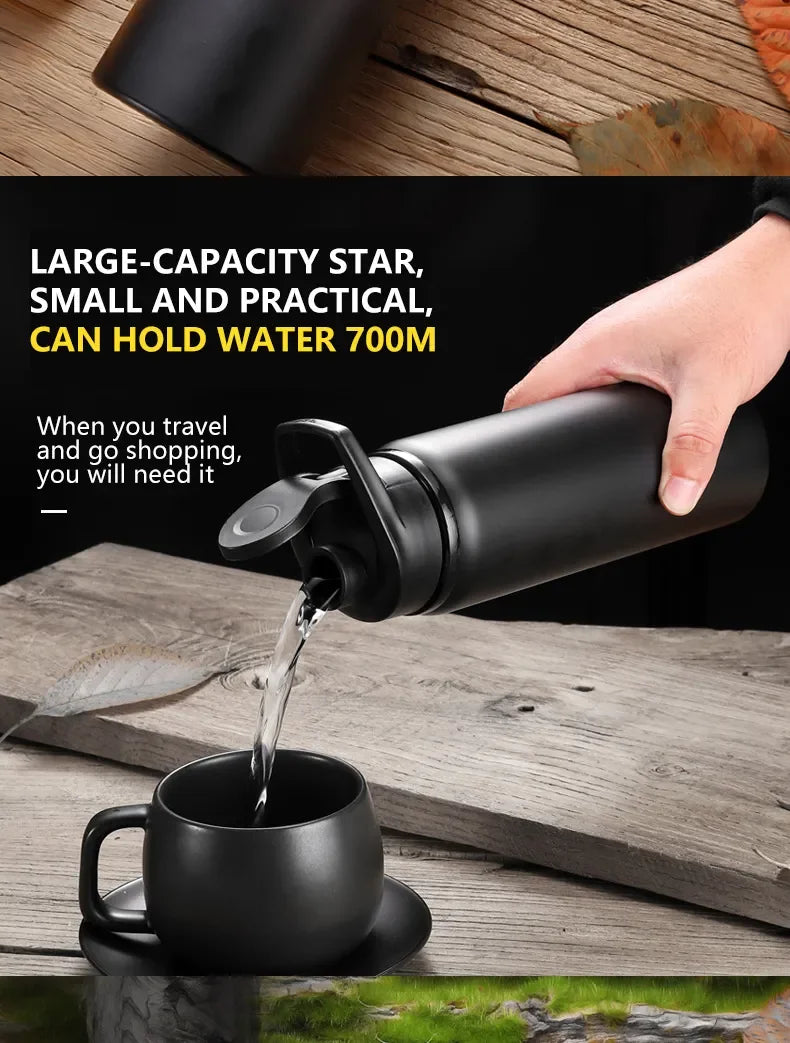 A black 700ml water bottle with a flip-top lid, being used to pour water into a matching black cup.