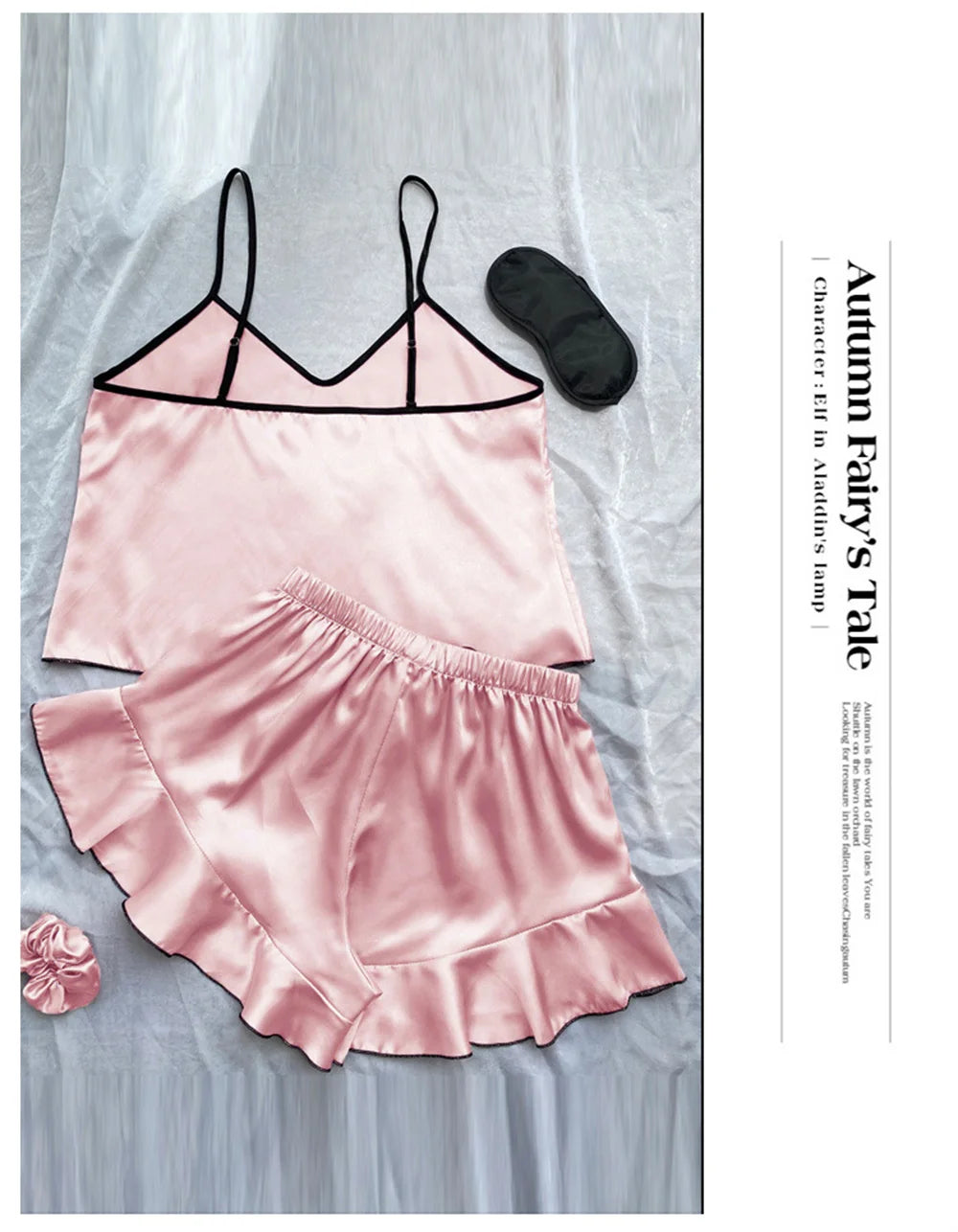 Pink satin camisole pyjama set with black trim, ruffled hem shorts, matching eye mask, and scrunchie.