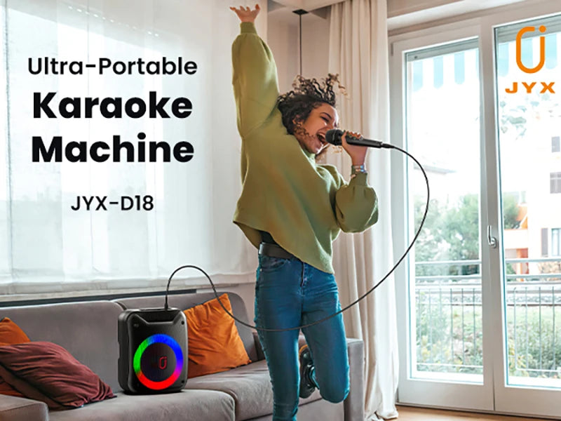 A person singing into a wired microphone next to a black portable speaker featuring a colourful circular LED light.