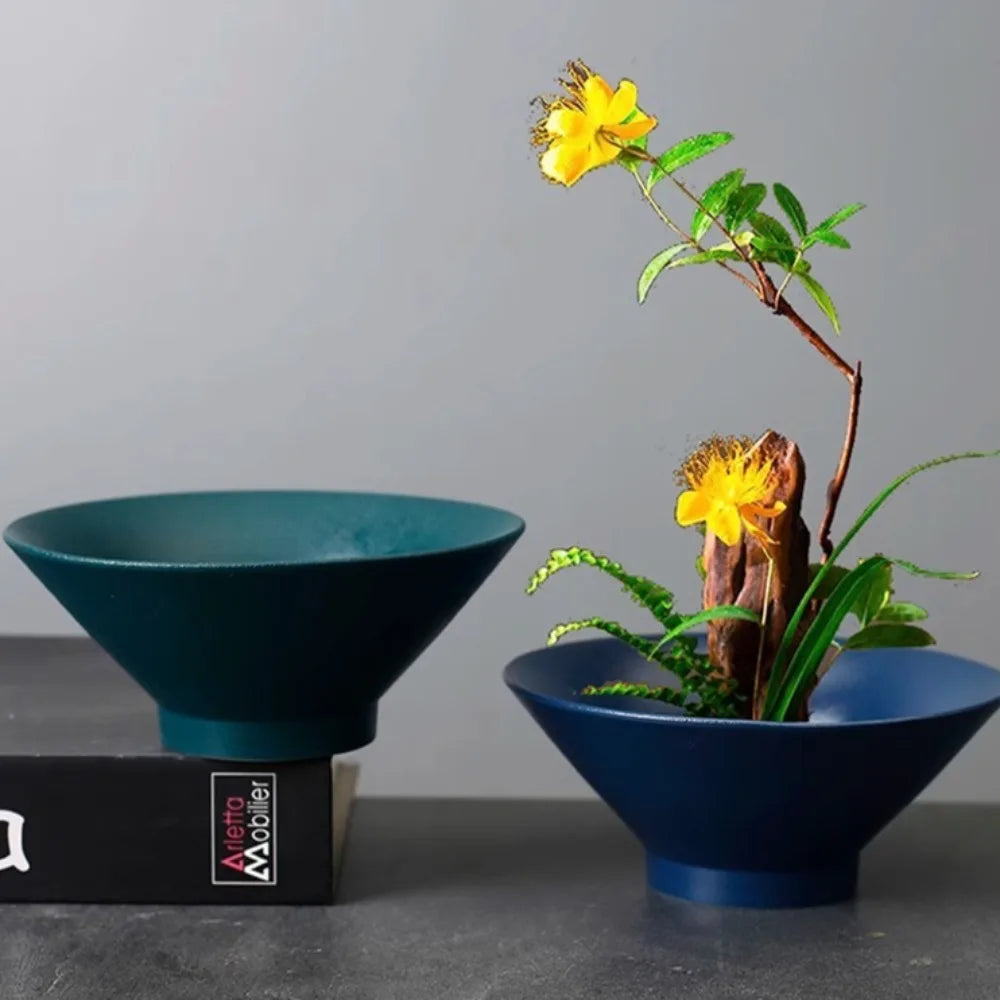 Two deep, cone-shaped ceramic bowls in dark teal and blue, one holding a floral arrangement with yellow flowers.