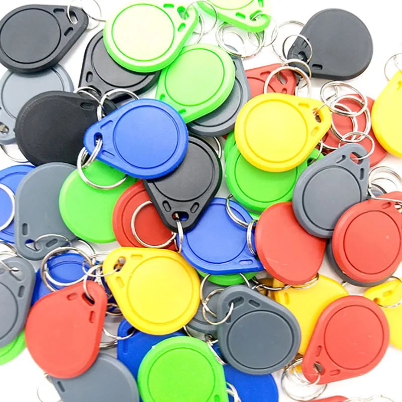 Pile of multicolored plastic RFID key fob tags with silver metal key rings on a white background.
