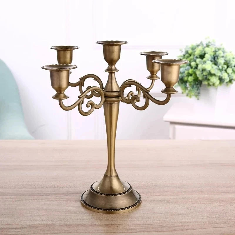 Bronze metal 5-arm candelabra featuring scrolled arms and a flared base on a wooden tabletop.