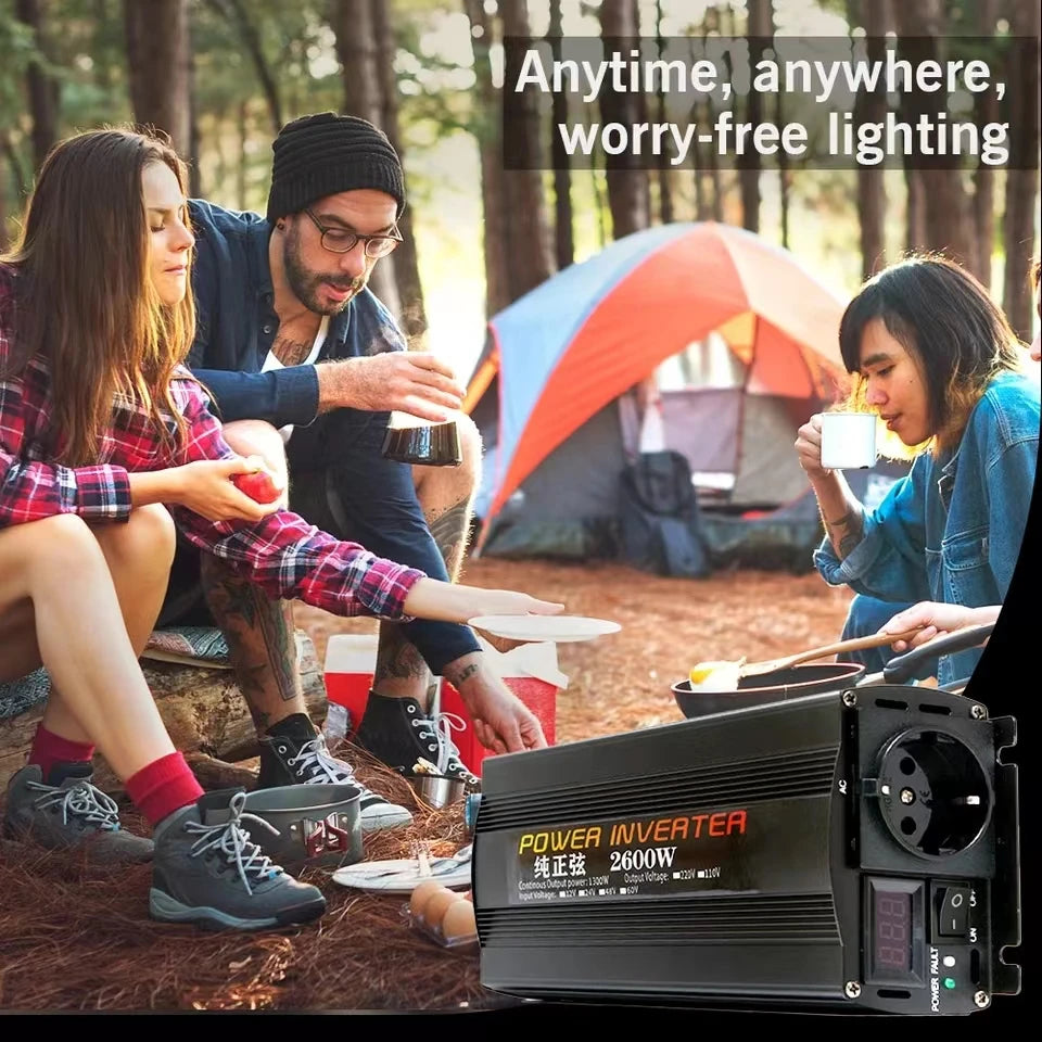 Black 2600W power inverter with digital display and AC socket, shown with friends camping in the woods.
